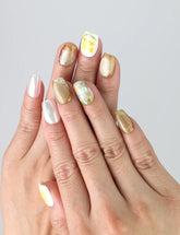 Hand wearing Naillover Nature's Glow press on nails with pastel floral prints and gold detailing for a soft, elegant effect.